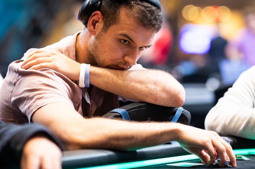 Michael Addamo at a poker table, stacks of chips in play, digital tournament screen in the background