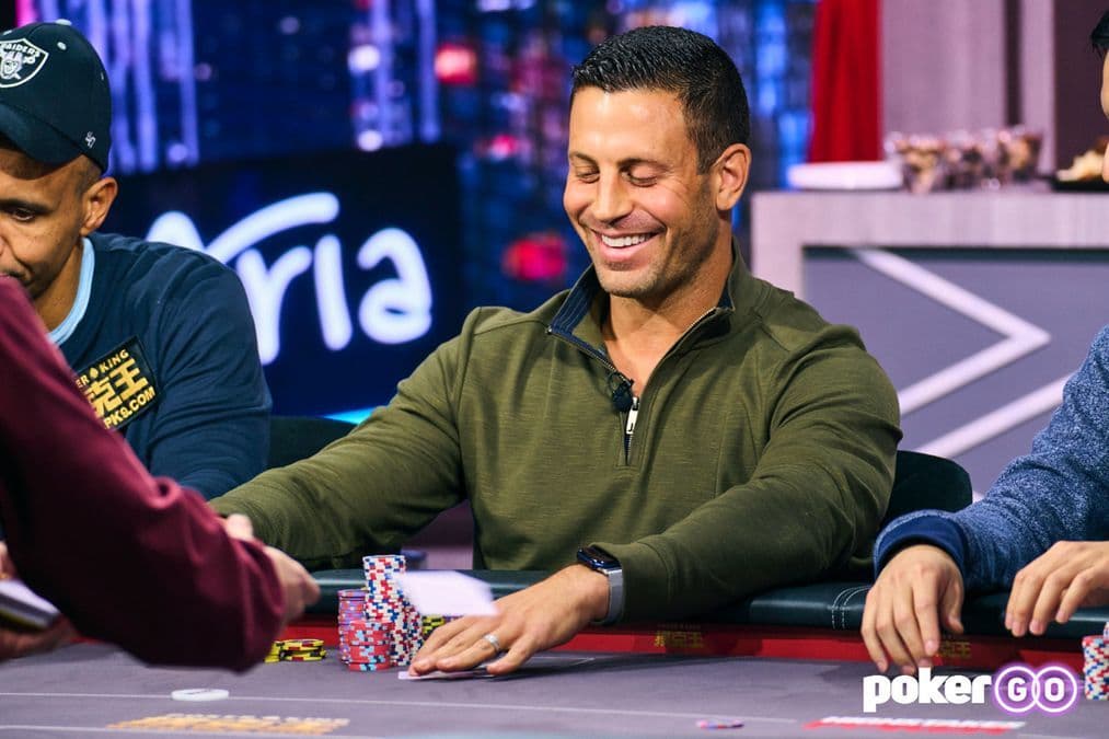 Garrett Adelstein at a poker table with a stack of books on a table, Commerce Casino in the background